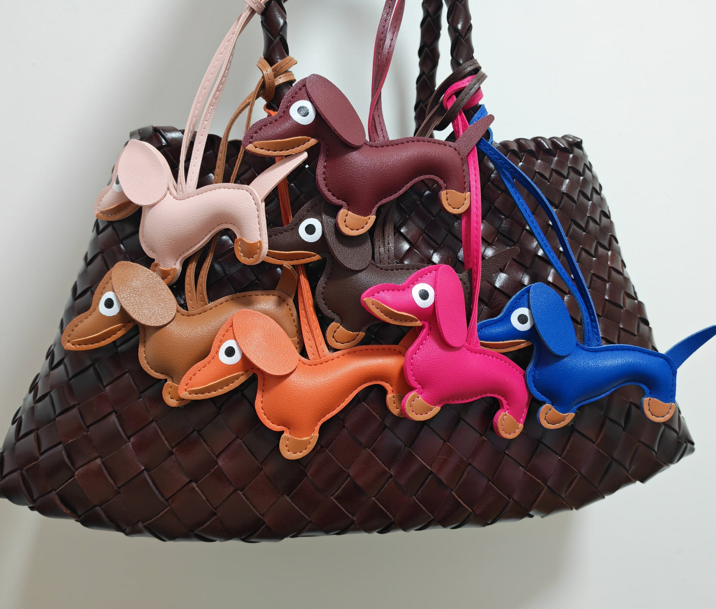 Handcrafted multicolor dachshund dog bag charms in faux leather hanging on a woven brown handbag