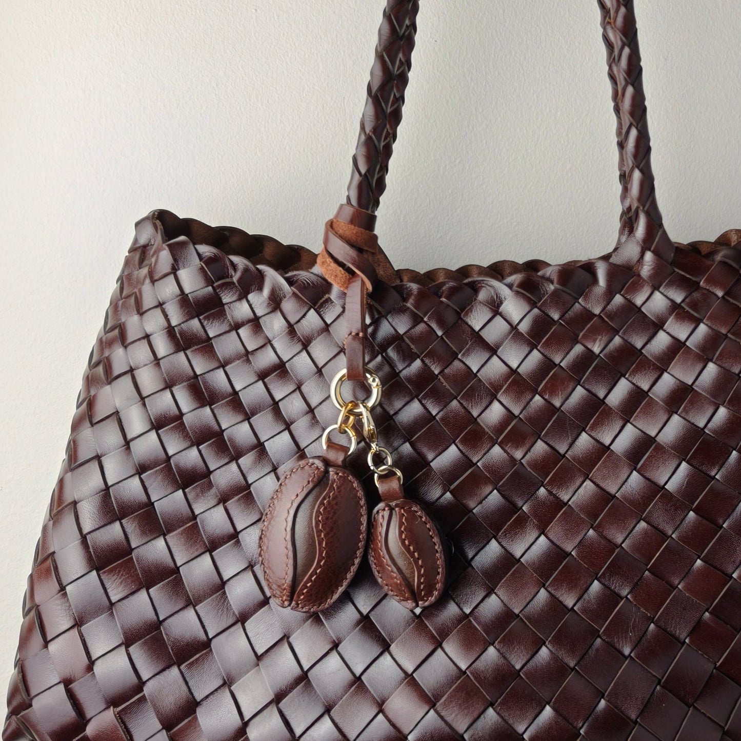Handmade coffee bean charm made of premium full grain leather attached to a woven brown leather handbag
