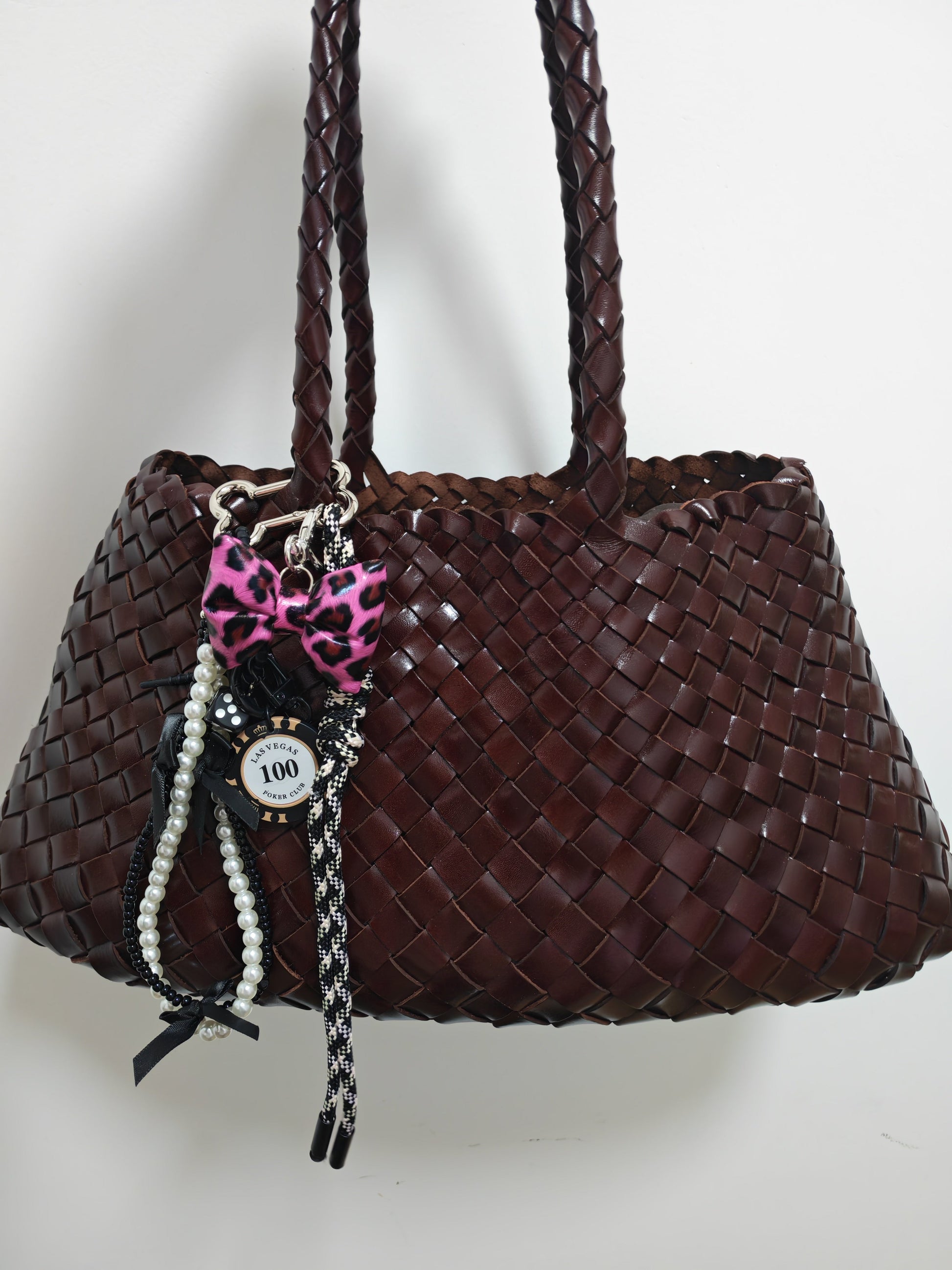Fiona Luxe Charm - Pink Leopard Bow Keychain with Pearl and Rope Details on a woven brown handbag.