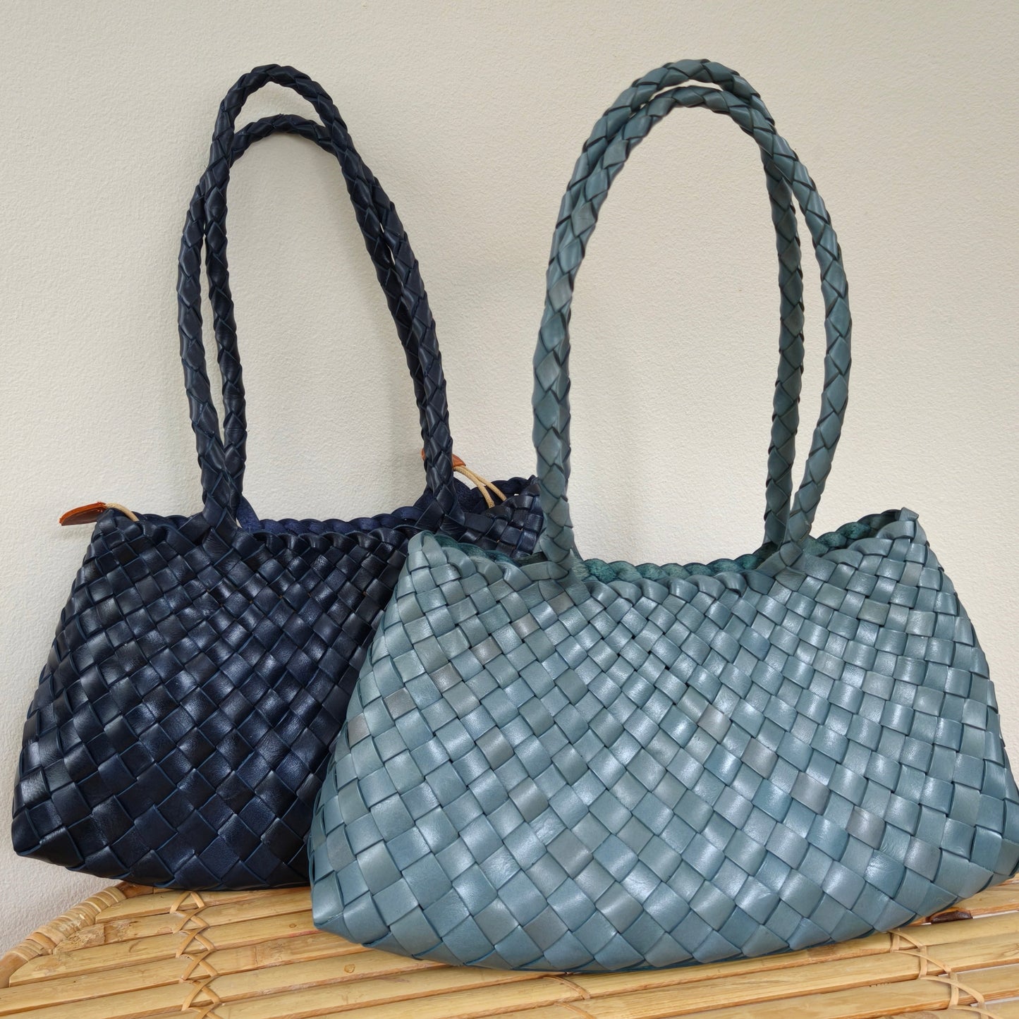 Two woven handbags, one black and one blue, on a bamboo surface with a light background.