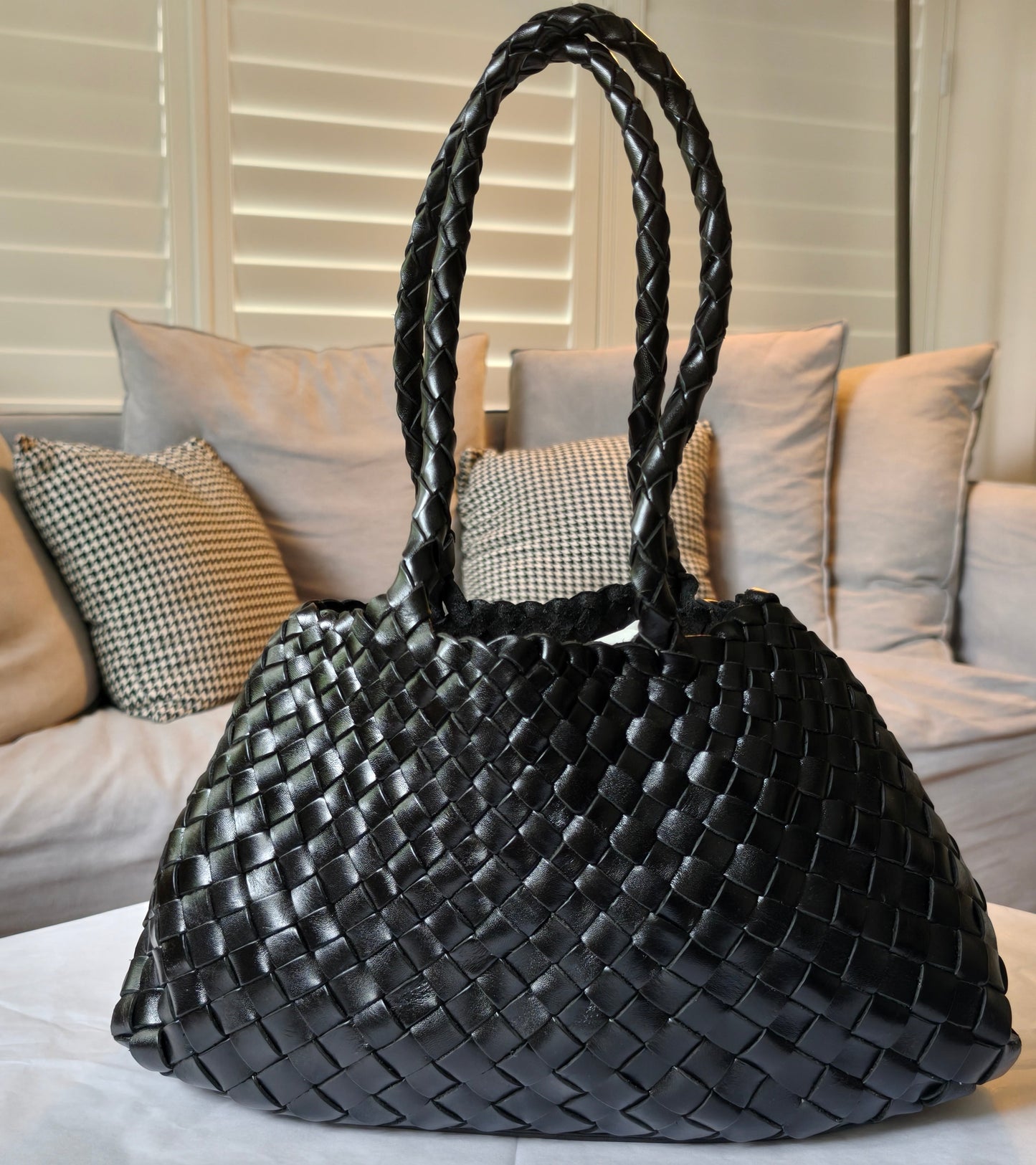 Black woven handbag on a light-colored couch with pillows
