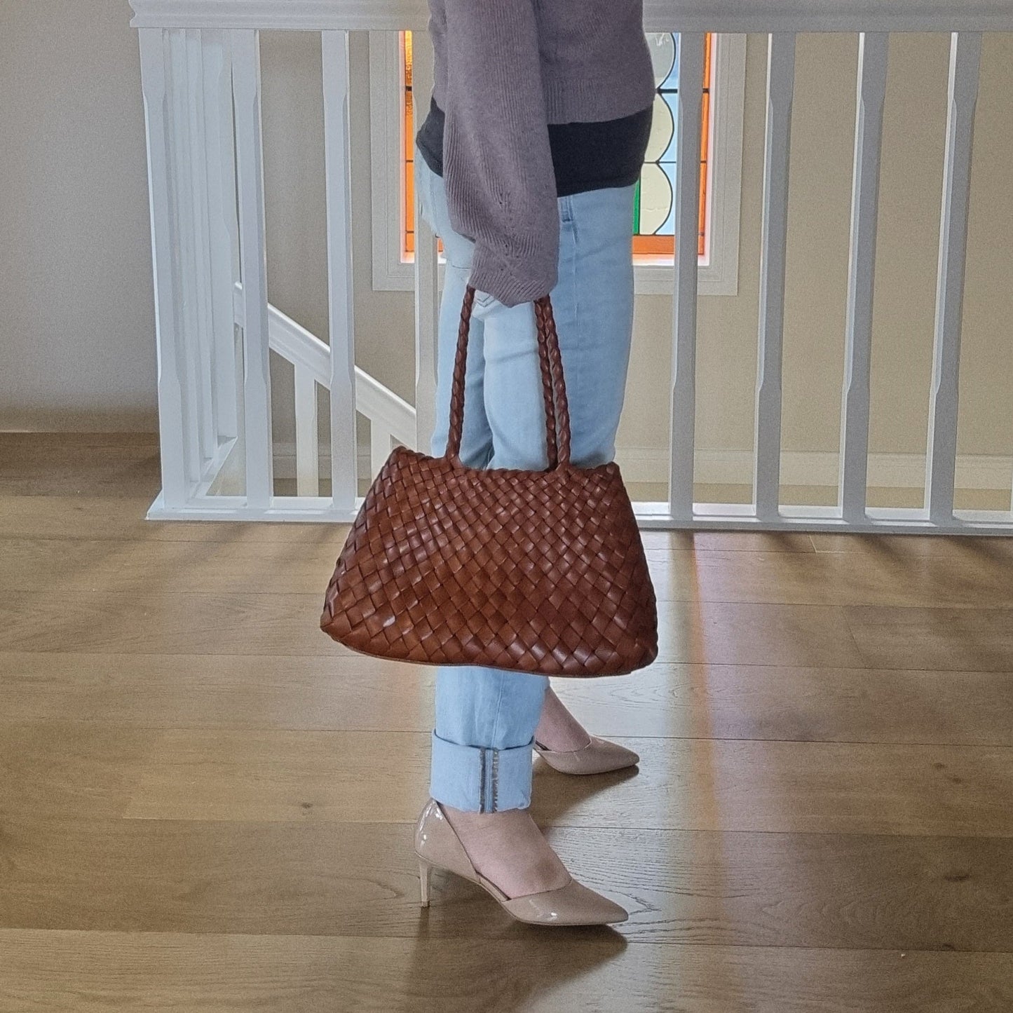 woman is holding a brown woven leather bag