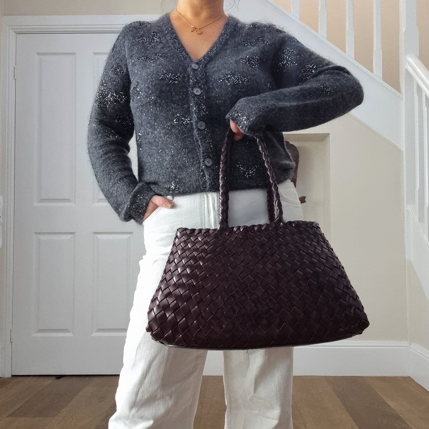 Woman holding Leah coffee leather woven tote bag in front of her body, showing medium long handles and structured woven texture