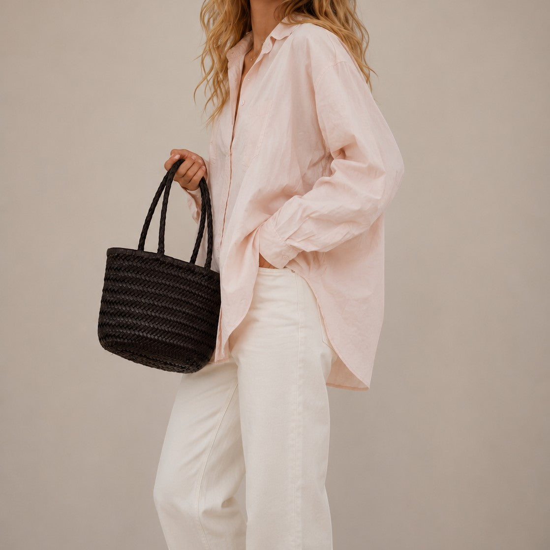 Woman holding a black woven handbag against a plain background