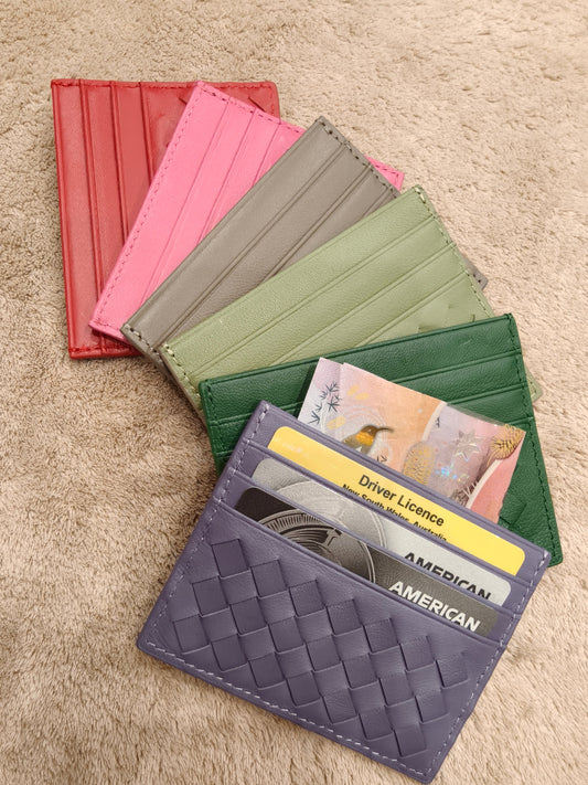 Woven leather card holder in multiple colors on a beige surface.