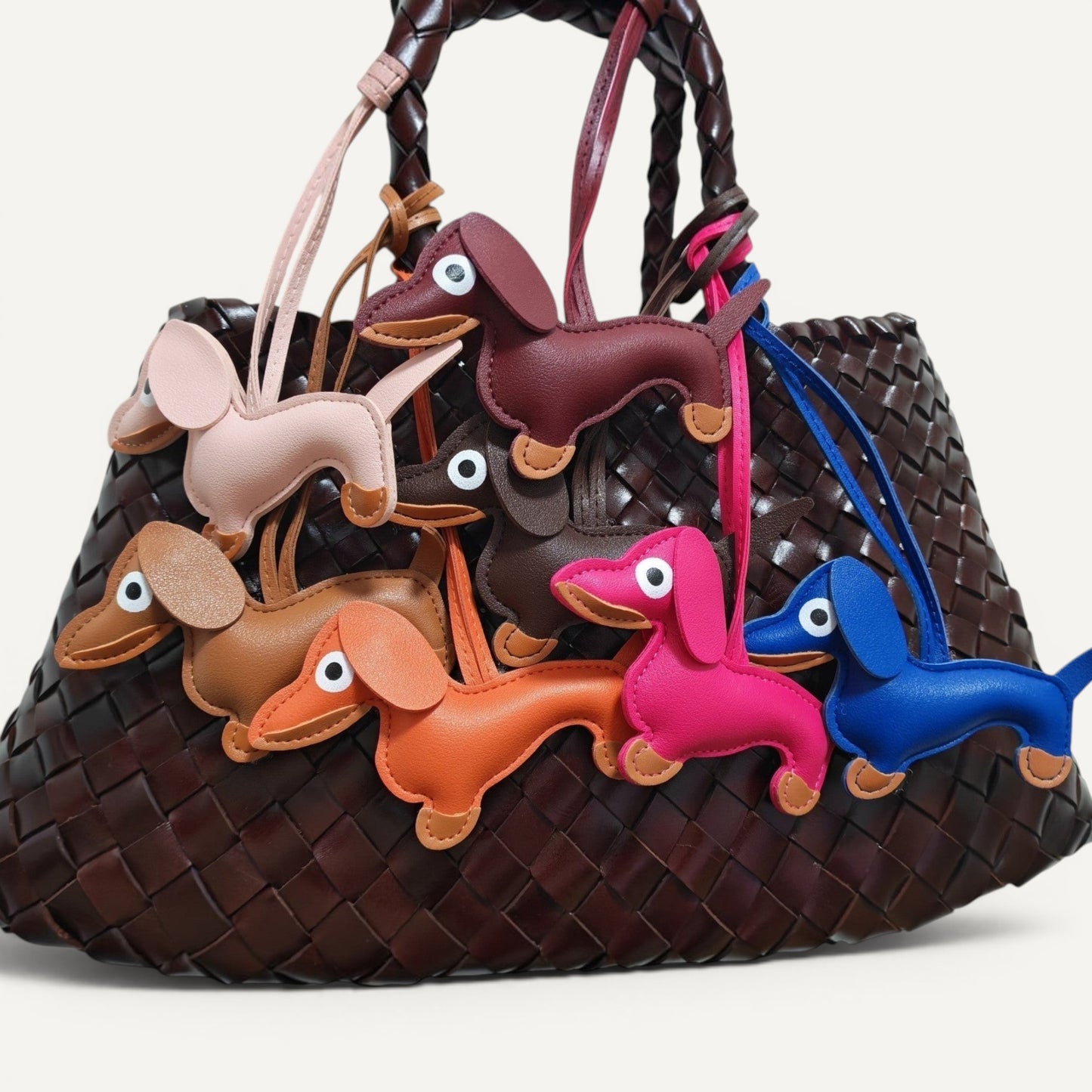 Handcrafted multicolor dachshund dog bag charms in faux leather hanging on a woven brown handbag