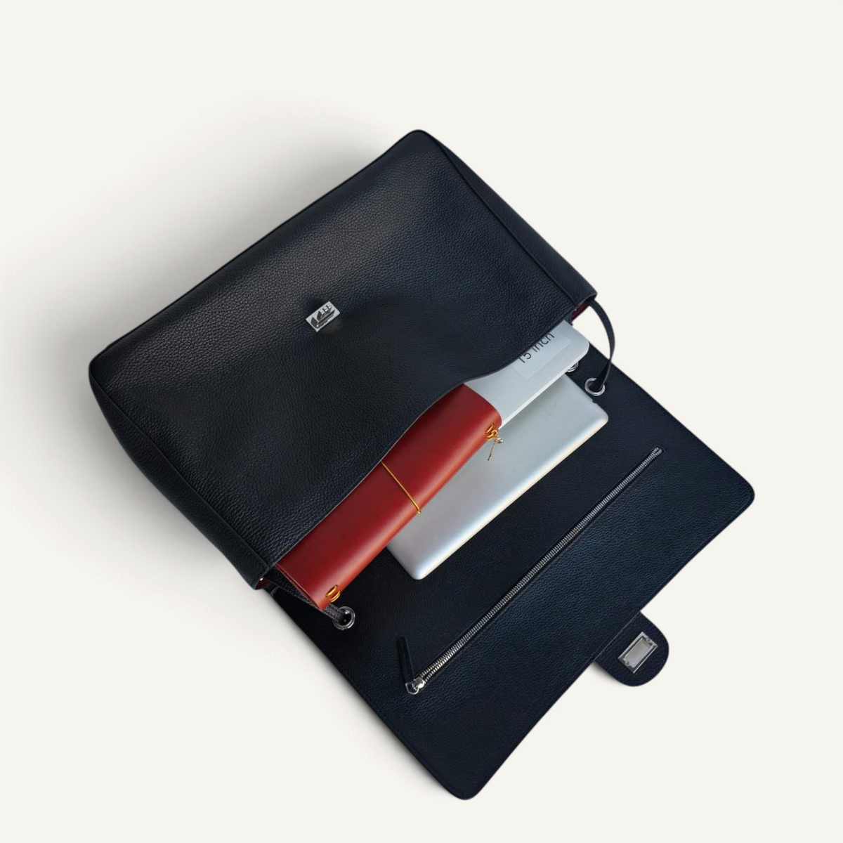 Fayecreations black leather laptop bag with a red notebook and silver laptop inside, featuring a metal clasp closure.