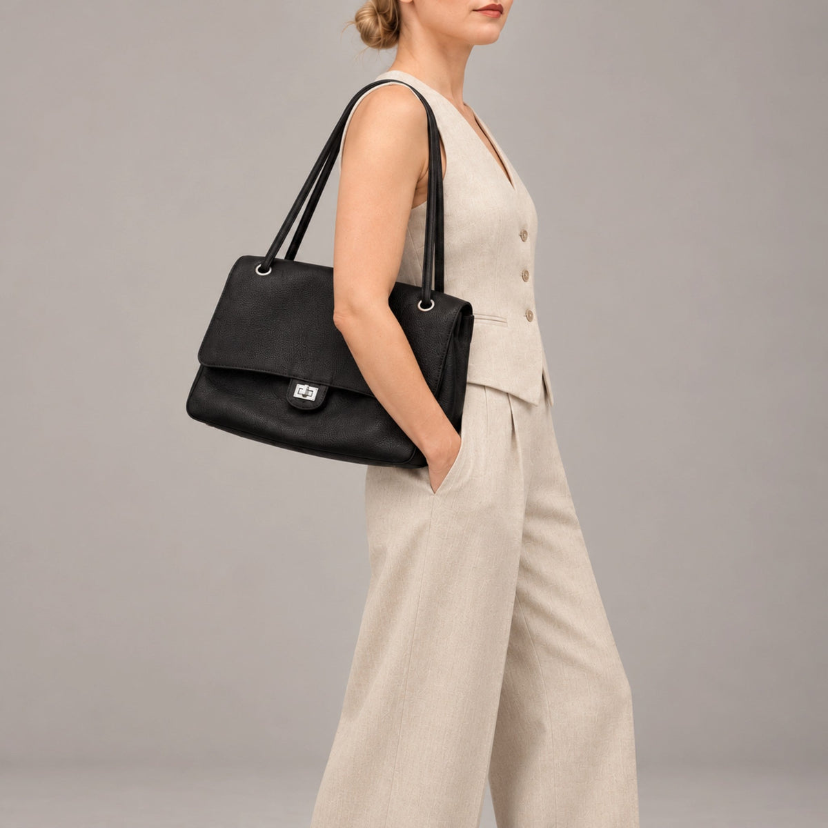 Fayecreations Eleanor large black genuine leather shoulder bag with turn-lock closure worn by a woman in a beige suit