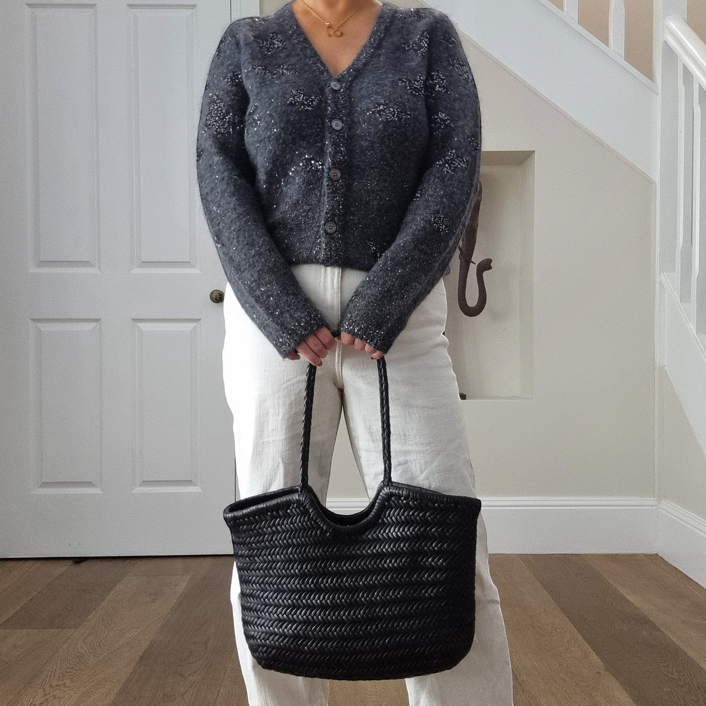 Large handmade genuine top layer cowhide woven leather shoulder bag in black, carried by person in gray sweater and white pants