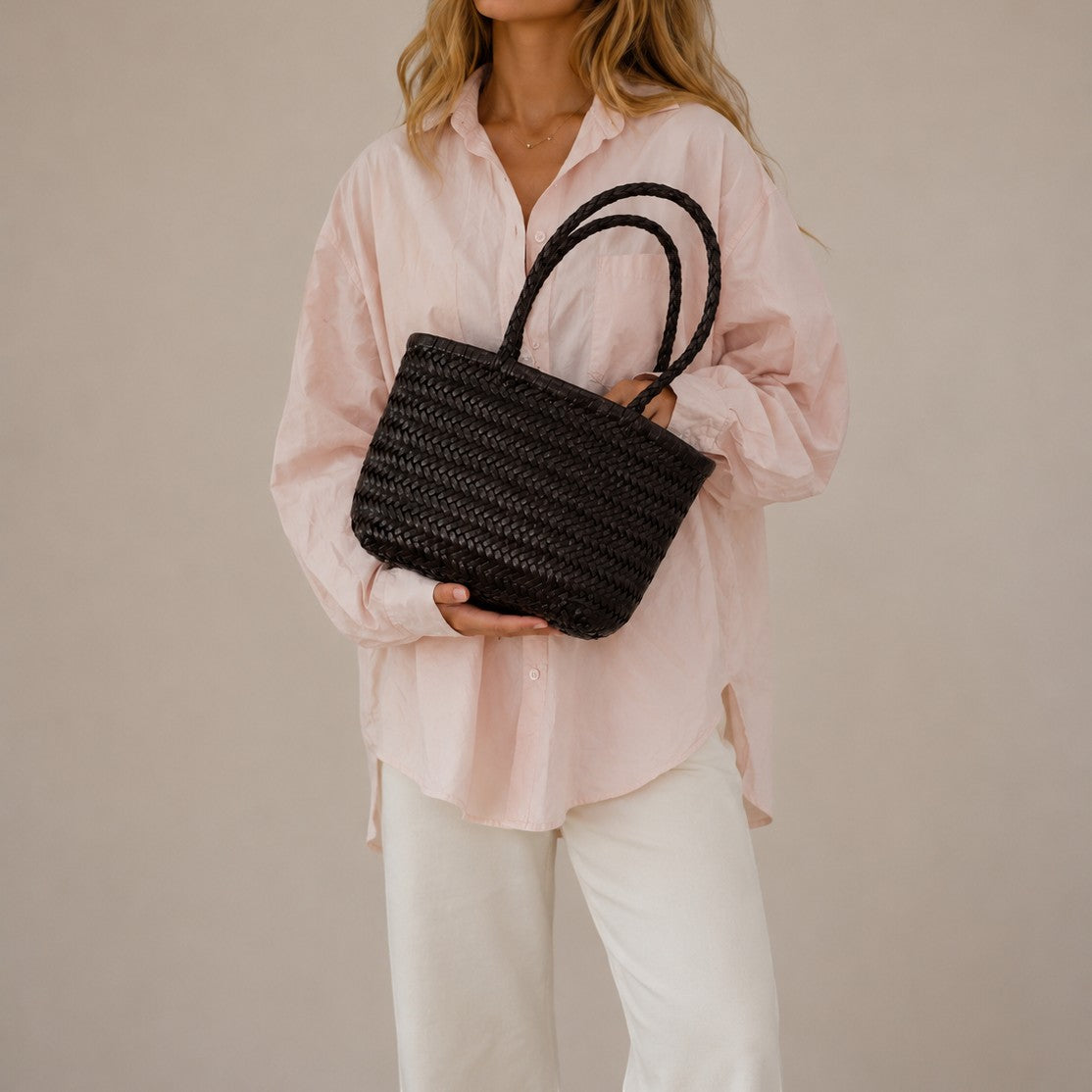 Woman holding a black woven handbag against a plain background