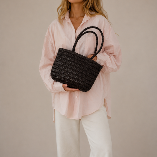 Woman holding a black woven handbag against a plain background