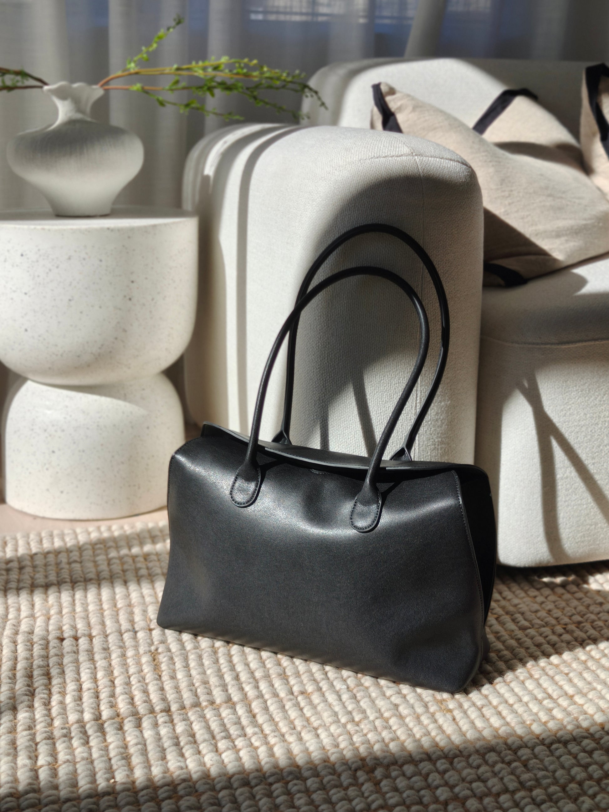 Black valentina leather handbag on a textured surface with a neutral background