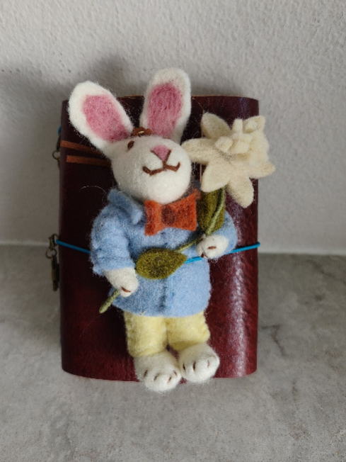 Felted rabbit decoration holding flowers on a cylindrical red object against a neutral background