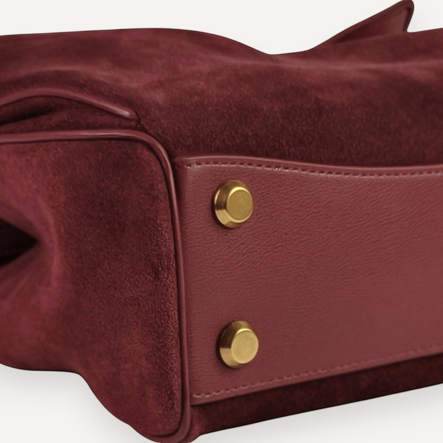 Close-up of a burgundy harper small handbag with gold buttons on a light gray background