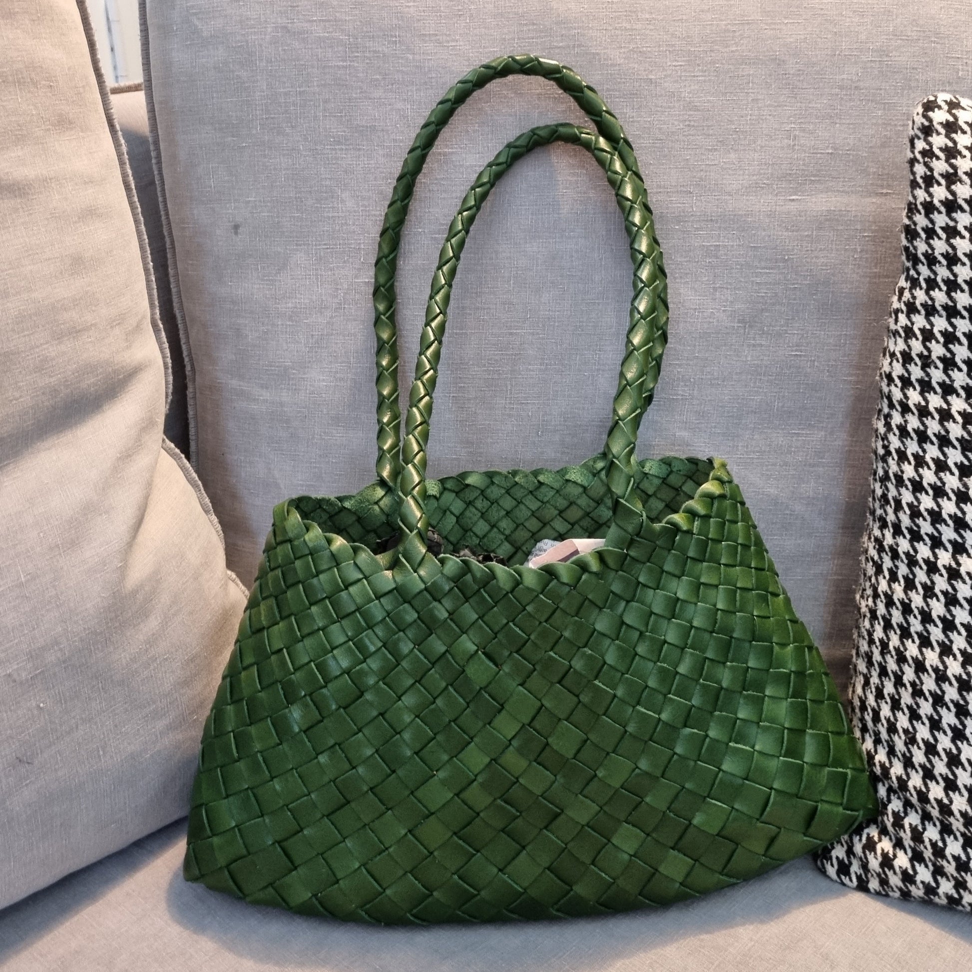 Handmade green cowhide leather woven shoulder tote bag with long handles on couch.