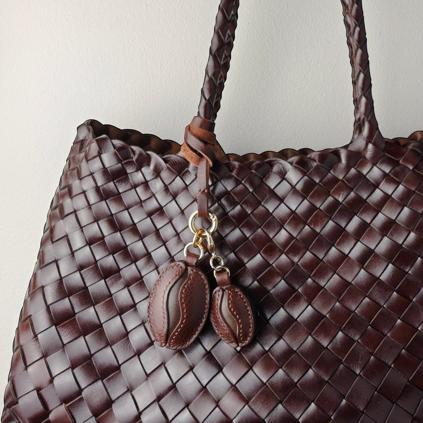 Handmade coffee bean charm made of premium full grain leather attached to a woven brown leather handbag