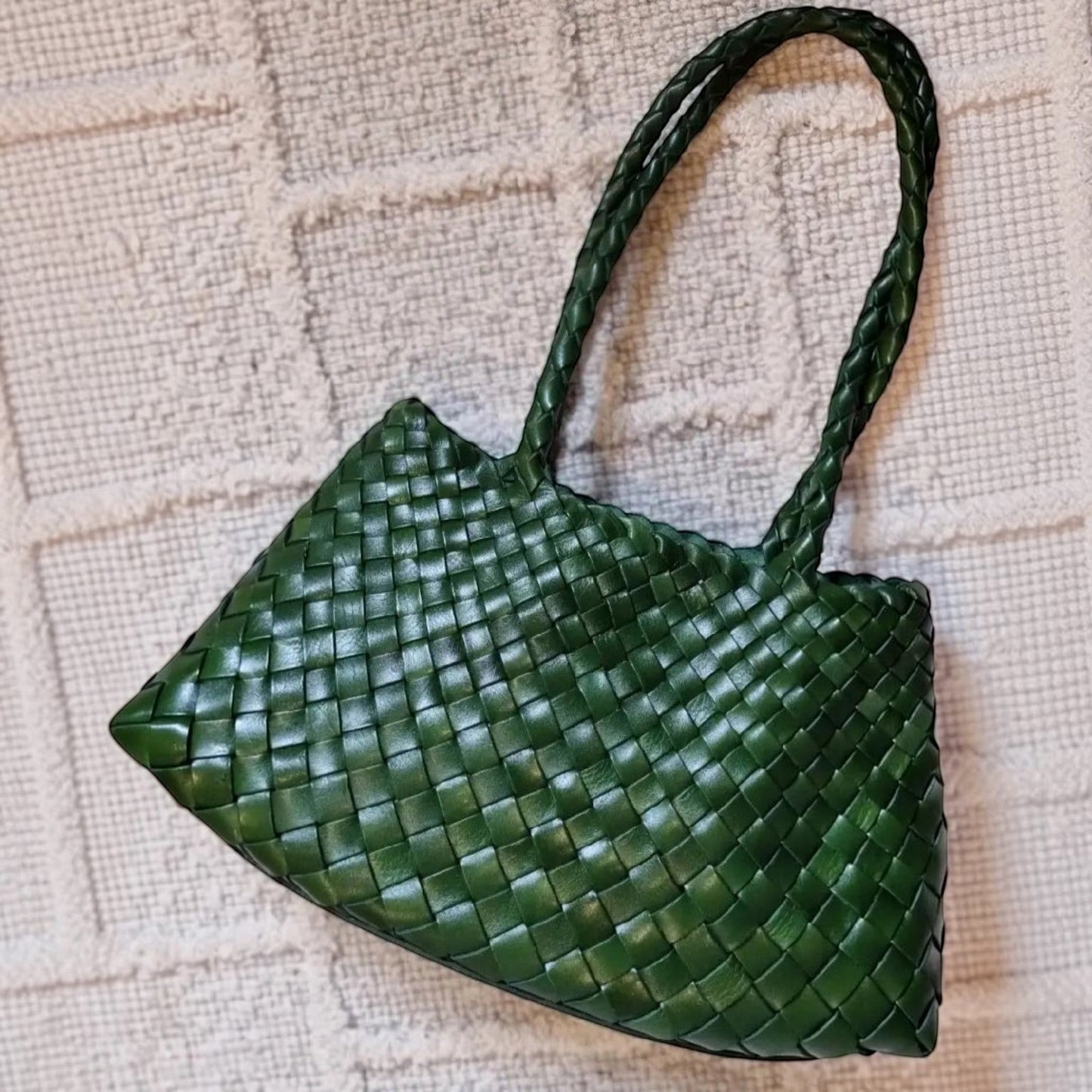 Green woven handbag on a textured beige surface