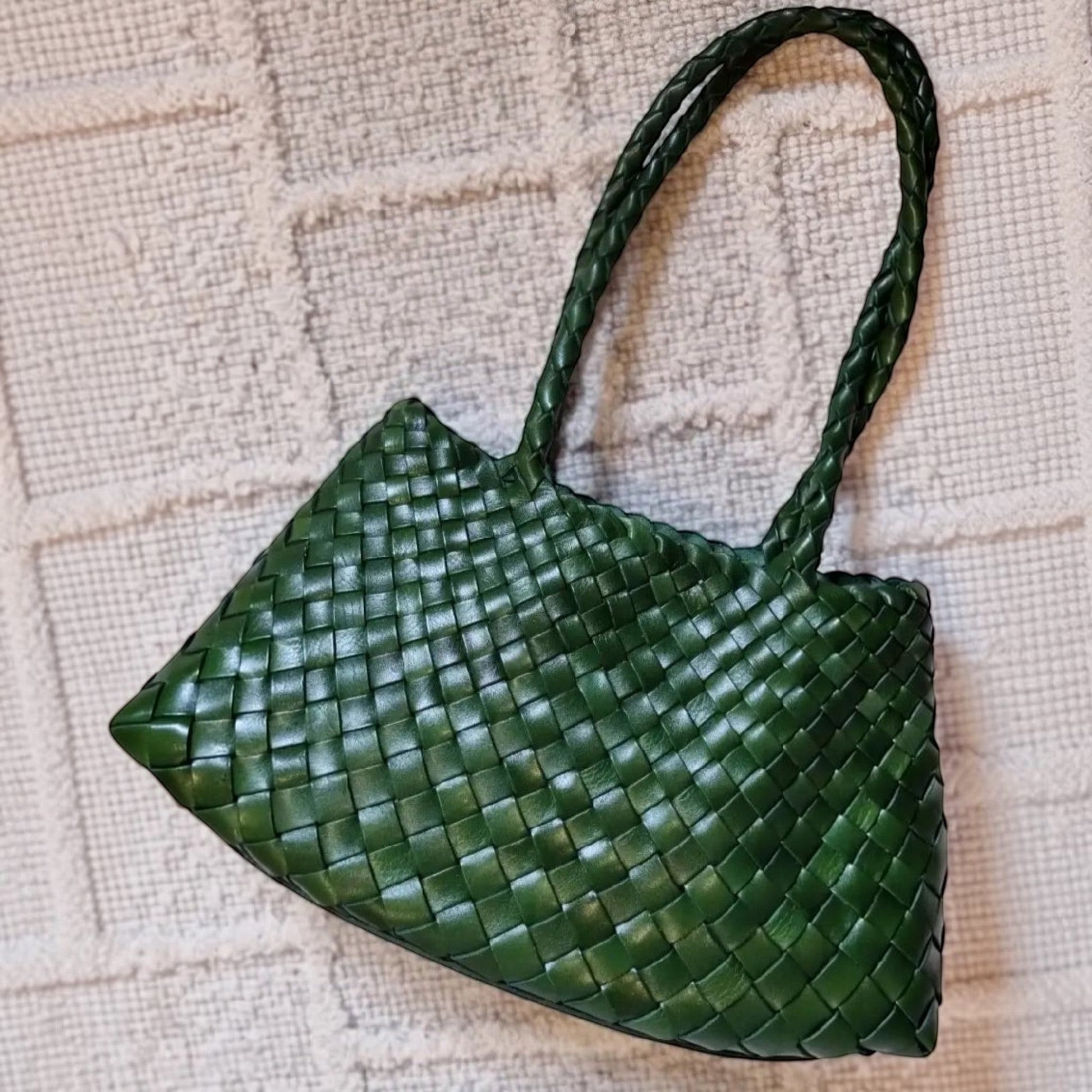 Green woven handbag on a textured beige surface