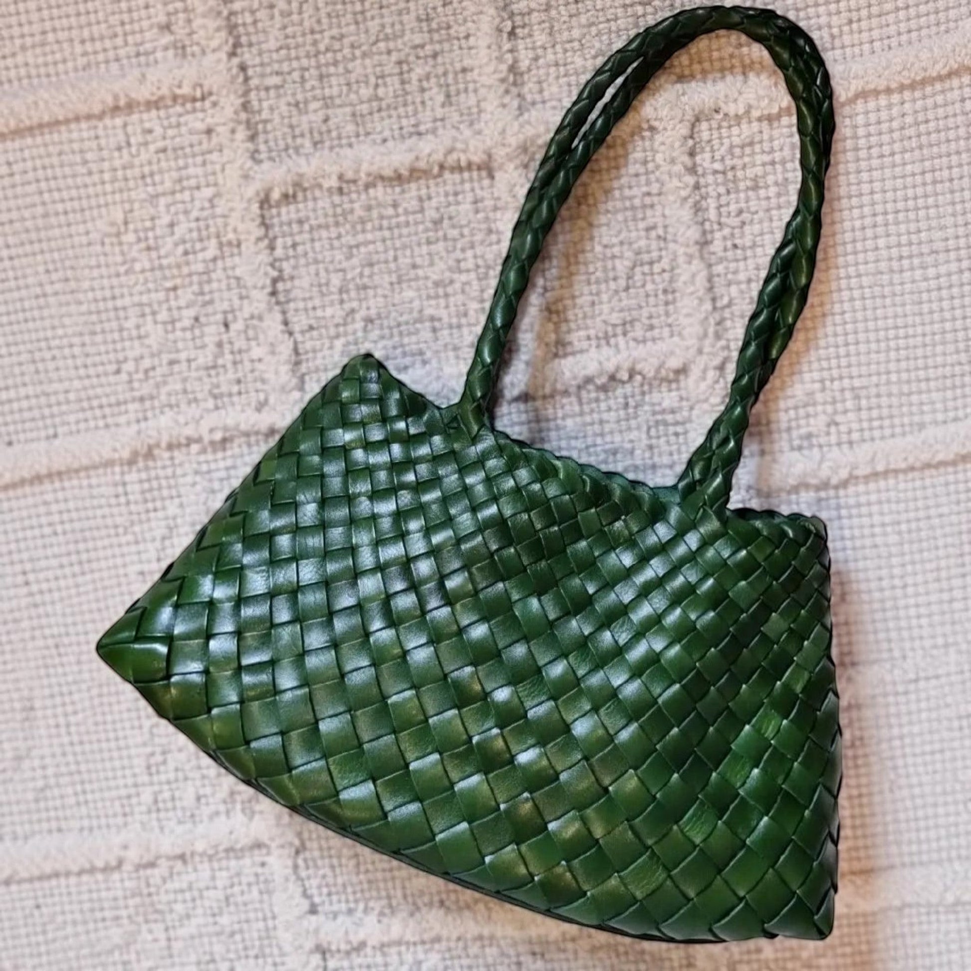 Green woven handbag on a textured beige surface