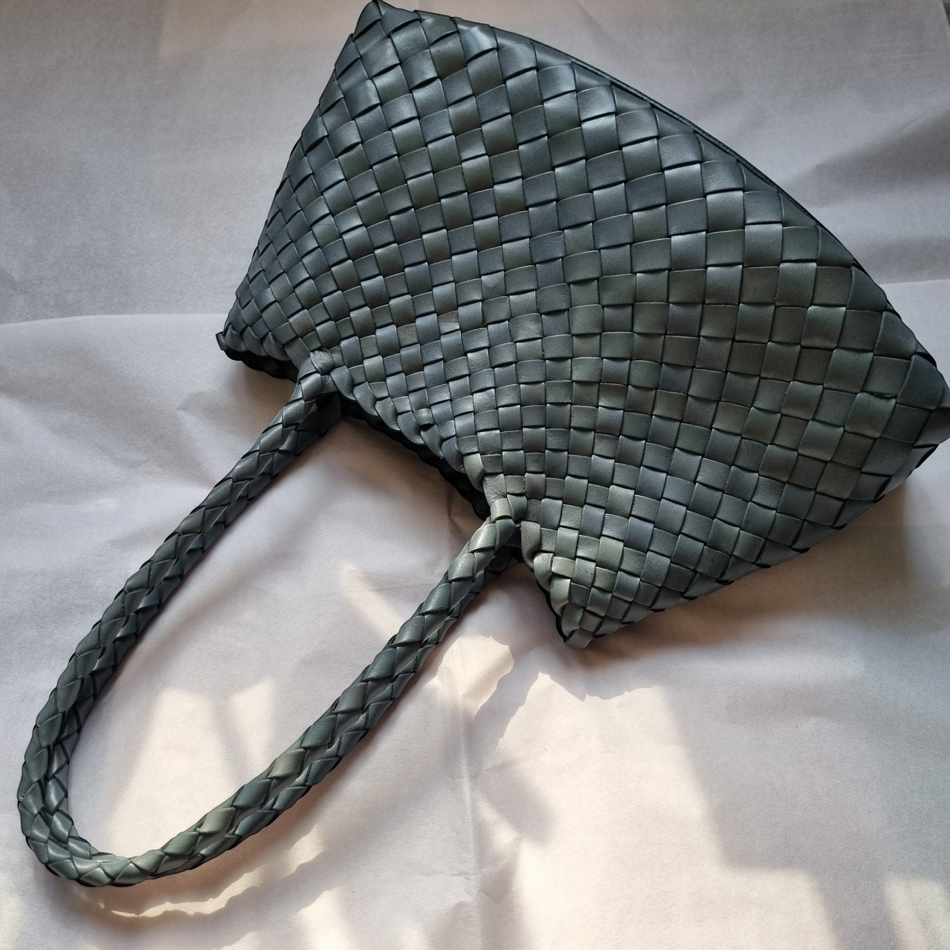 Opal leather woven bag lying on white fabric background, showing woven texture and soft leather finish