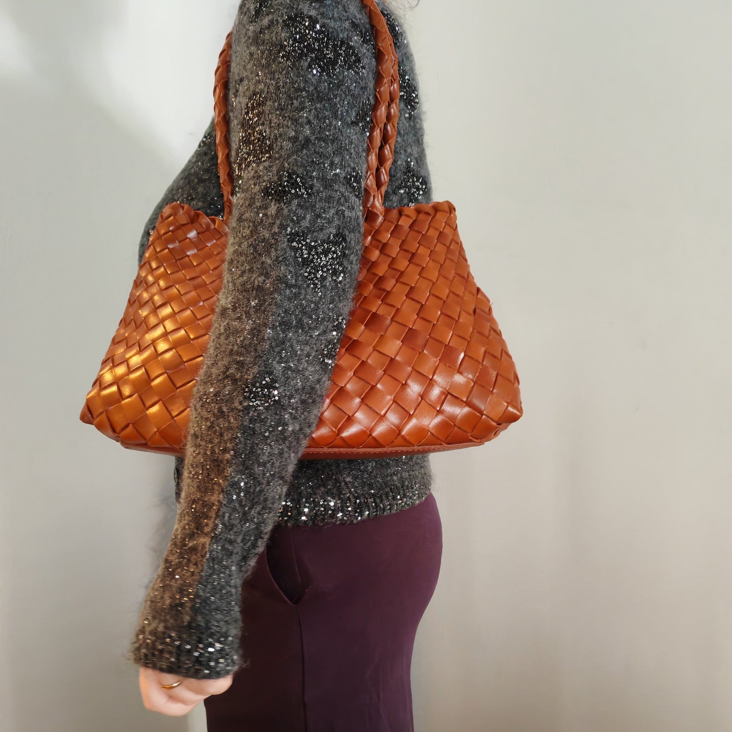 Person carrying a woven brown handbag on shoulder against a neutral background