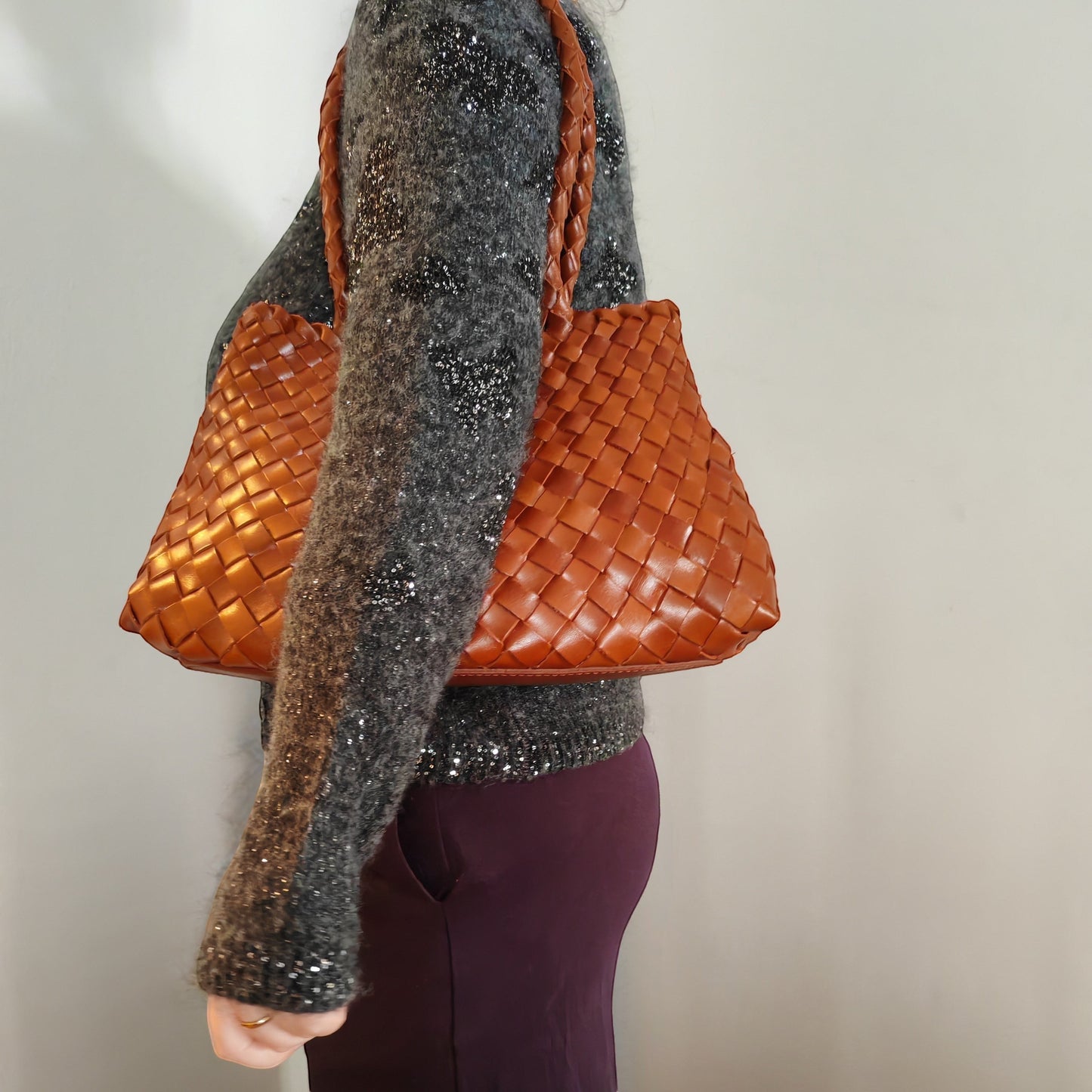 Person carrying a woven brown handbag on shoulder against a neutral background