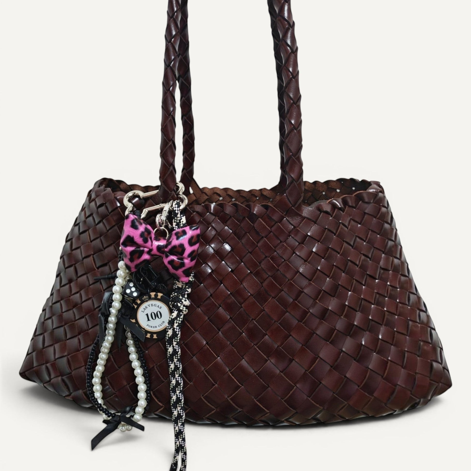 Fiona Luxe Charm - Pink Leopard Bow Keychain with Pearl and Rope Details on a woven brown handbag.