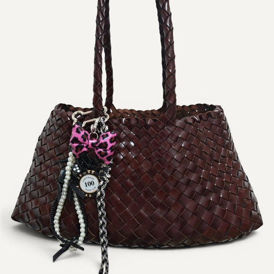 Fiona Luxe Charm - Pink Leopard Bow Keychain with Pearl and Rope Details on a woven brown handbag.