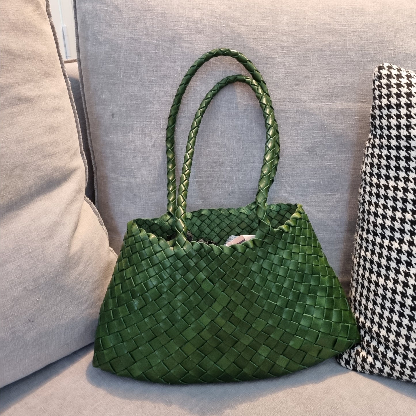 Handmade green cowhide leather woven shoulder tote bag with long handles on couch.