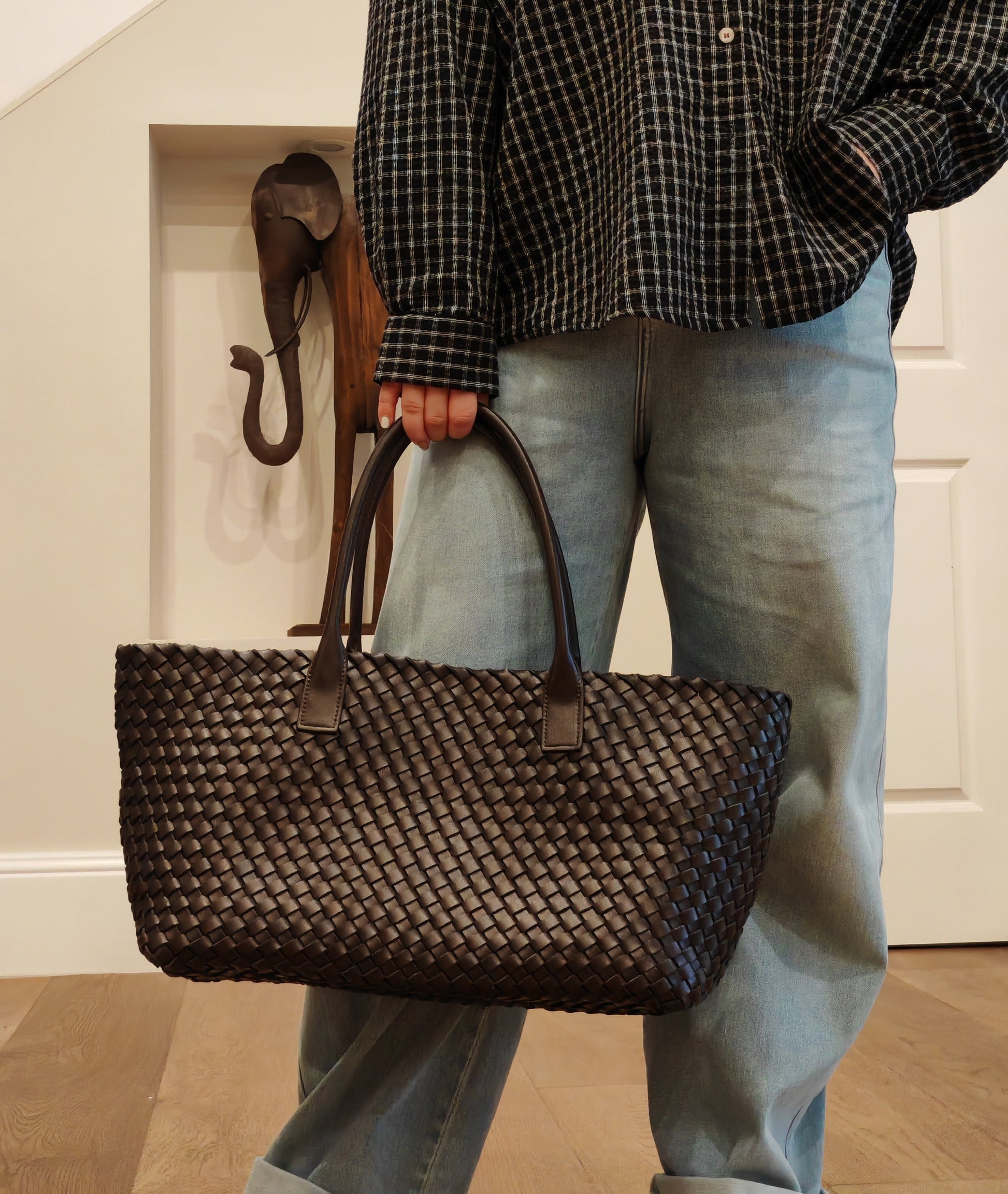 June Large Leather Woven Tote in black with premium cowhide and microfiber leather handles, carried by a person in jeans indoors.
