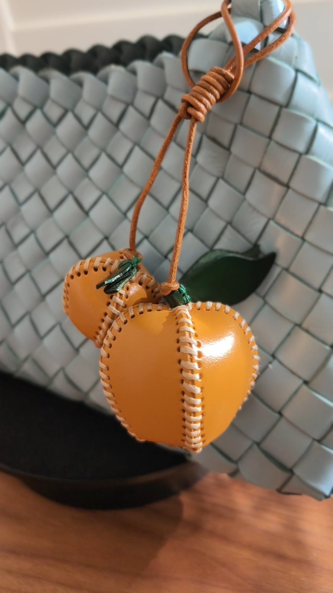 Apple Charm accessory on a woven handbag.