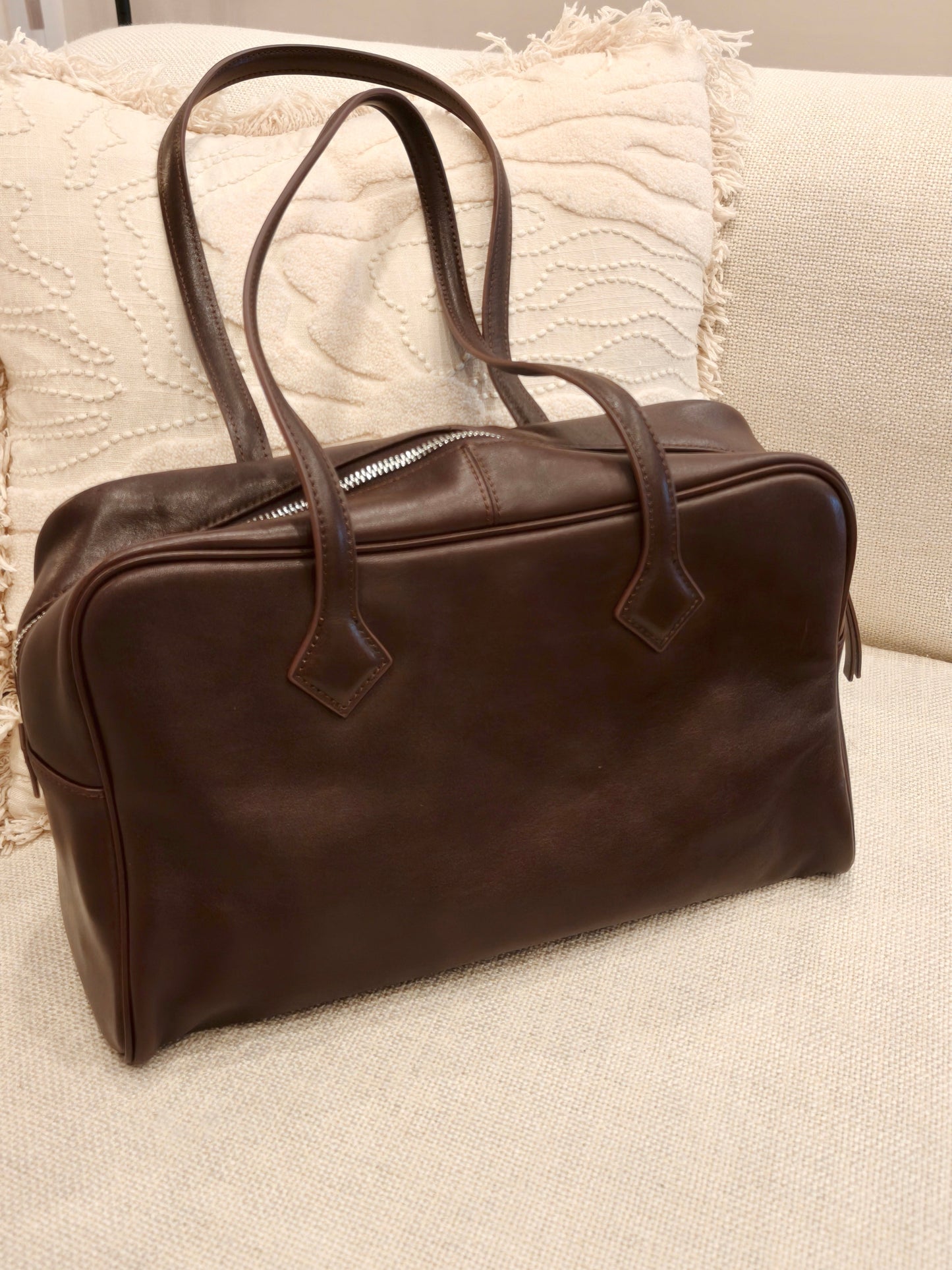 Full-grain leather commuter and laptop tote, with zippered compartments, on a beige couch.