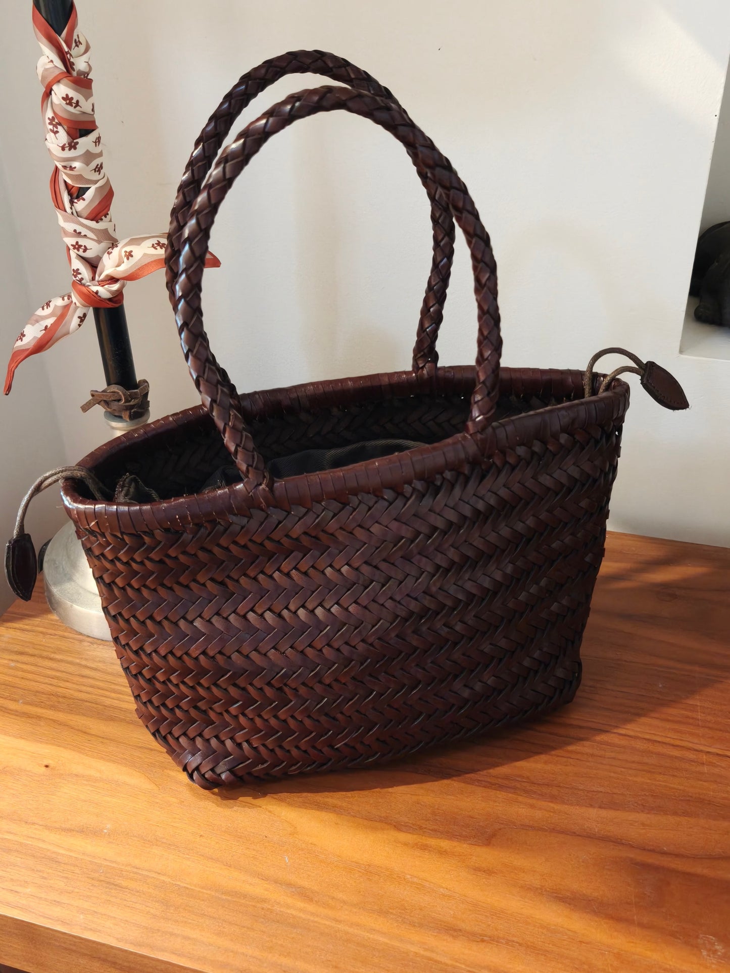 Handmade genuine cowhide woven leather shoulder bag on wooden table.