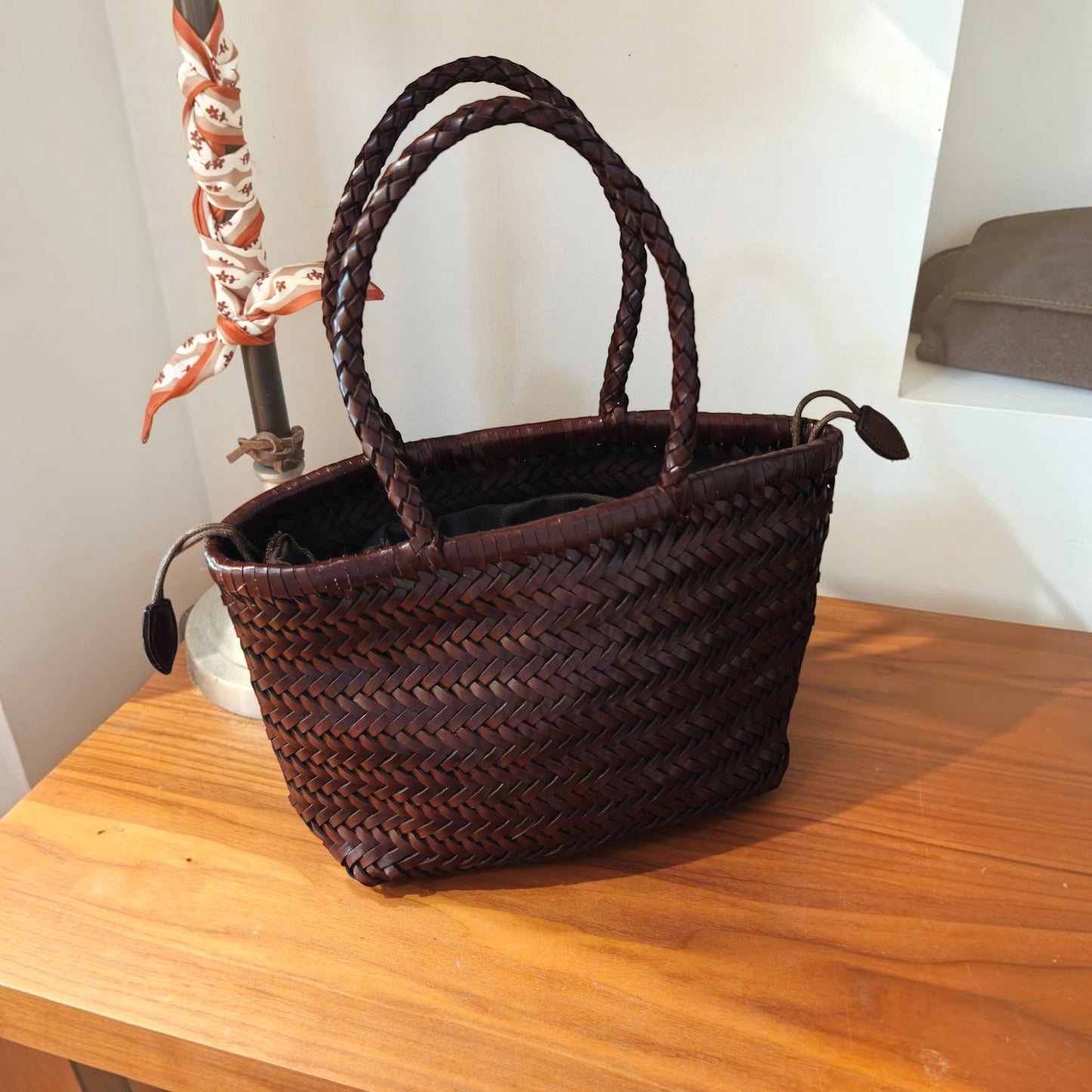 Handmade genuine cowhide woven leather shoulder bag on wooden table.
