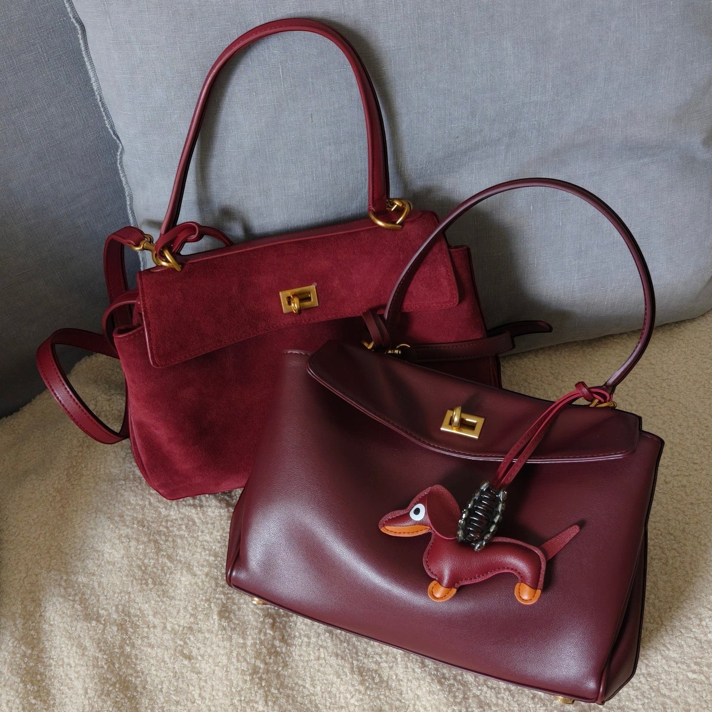 Two burgundy colour harper handbags with a small dog charm on a textured surface.