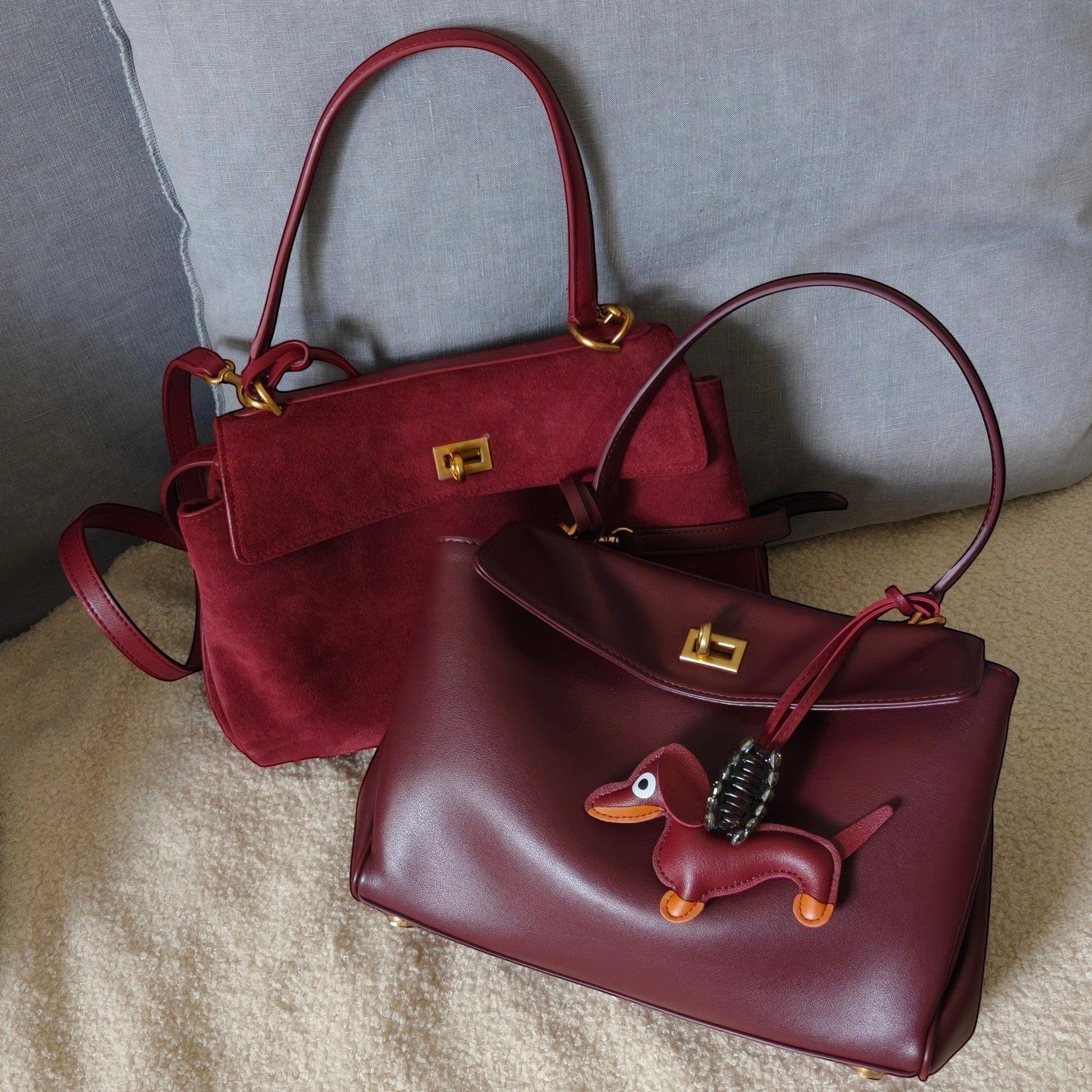 Two burgundy colour harper handbags with a small dog charm on a textured surface.