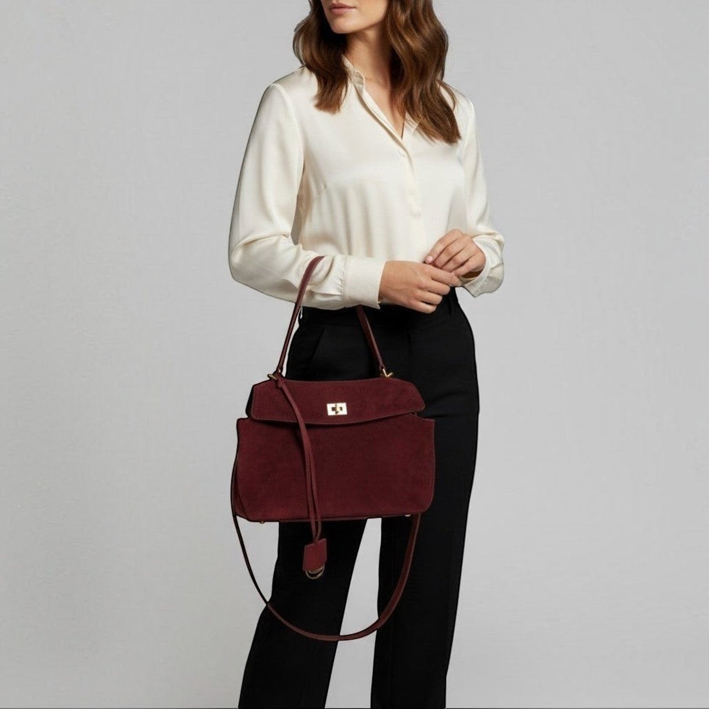 Woman holding a happer burgundy handbag against a plain background