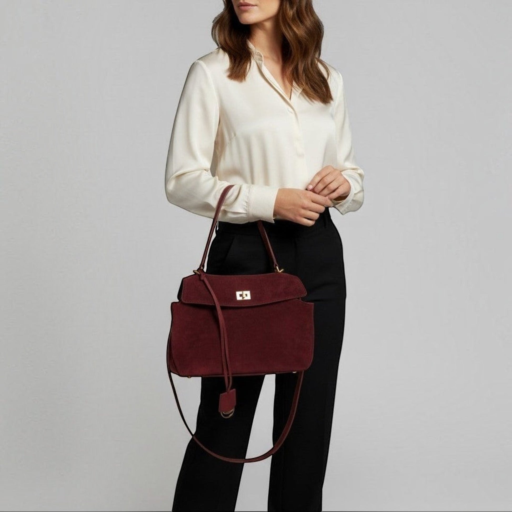 Woman holding a happer burgundy handbag against a plain background