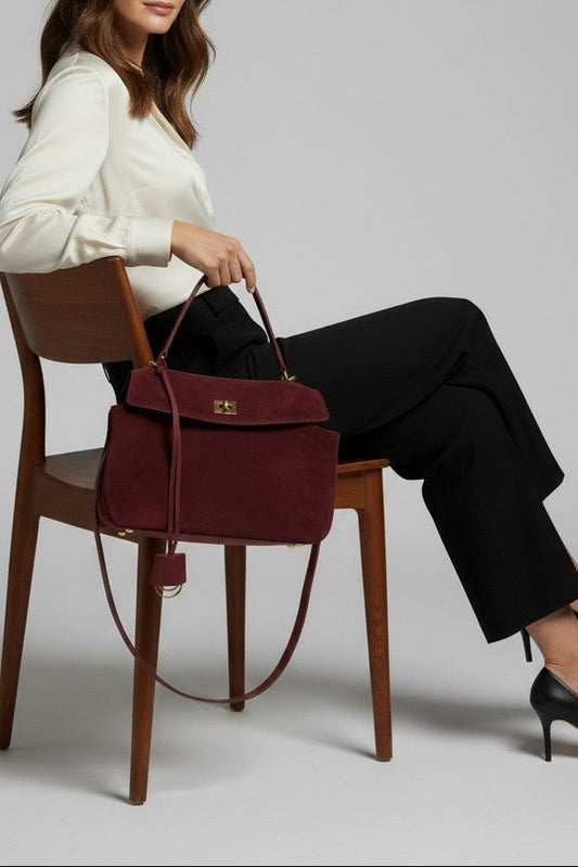 Woman sitting on a chair holding a maroon handbag against a plain background